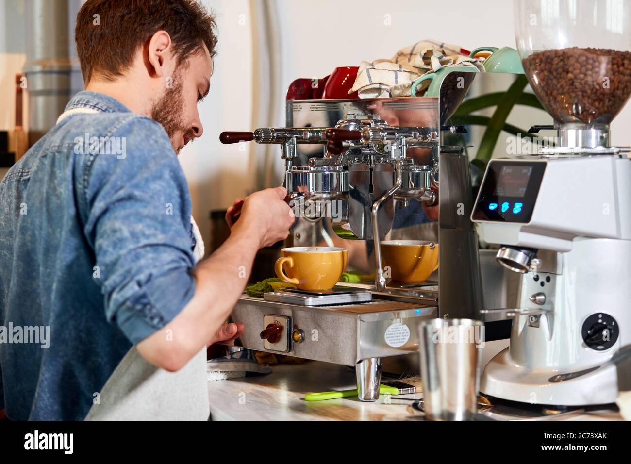 El proceso de trabajo de un hábil barman en la cafetería, el joven toca la  máquina de café, espera a que el café fresco sea poored, complets orden de  cu Fotografía de