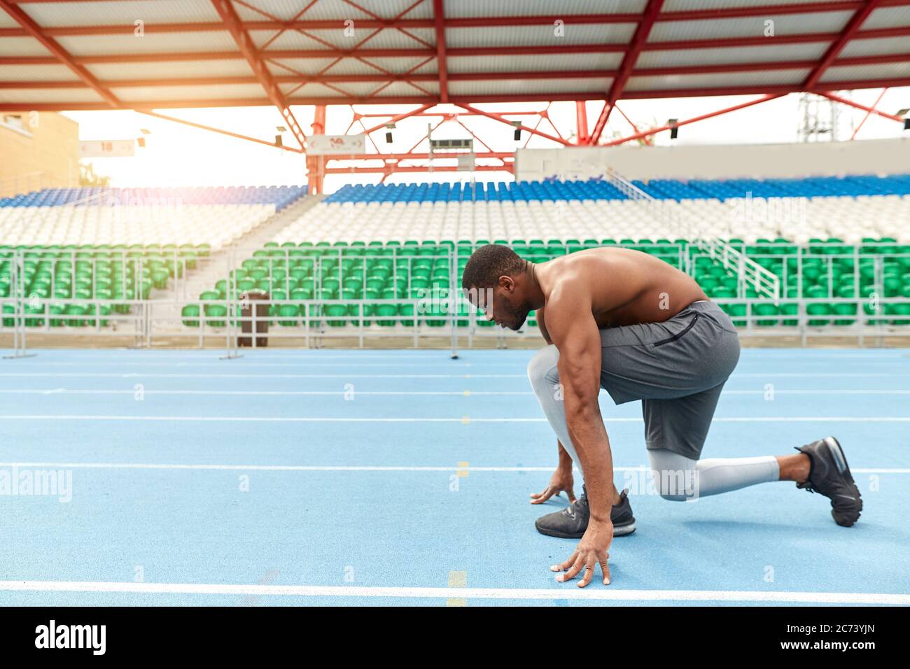 el talentoso corredor africano está listo para sprint, hombre parado en la posición de inicio bajo, foto de vista lateral completa. espacio de copia Foto de stock