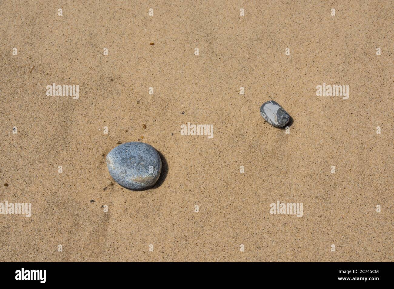 Dos guijarros suaves de playa sobre un fondo de arena lavada con agua plana Foto de stock