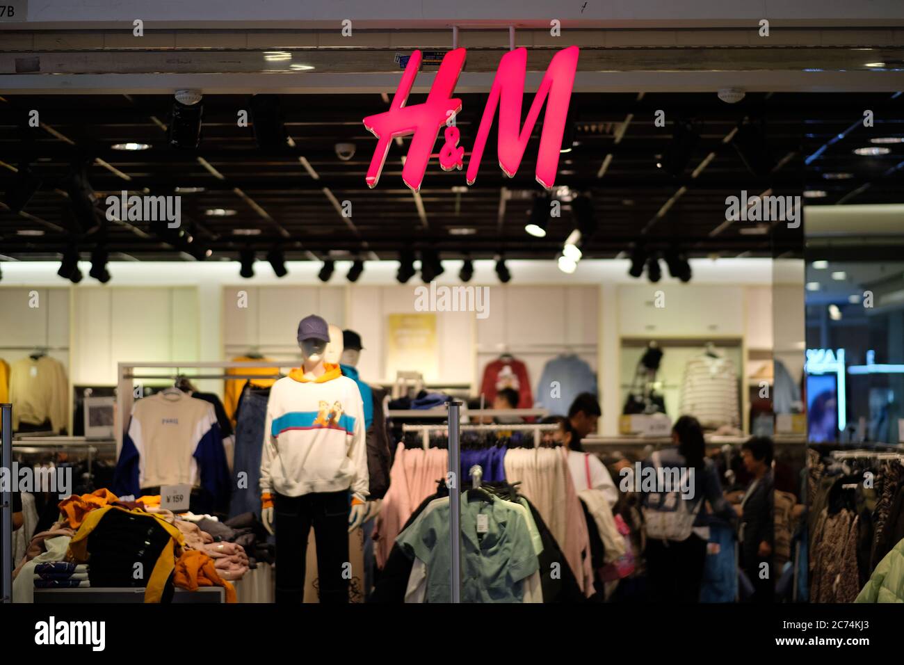 Fachada de la tienda de ropa H&M. Logotipo rojo brillante colgado en la entrada. Desenfoca la tienda de ropa y los clientes como fondo. Una Marca de moda sueca Fotografía de stock