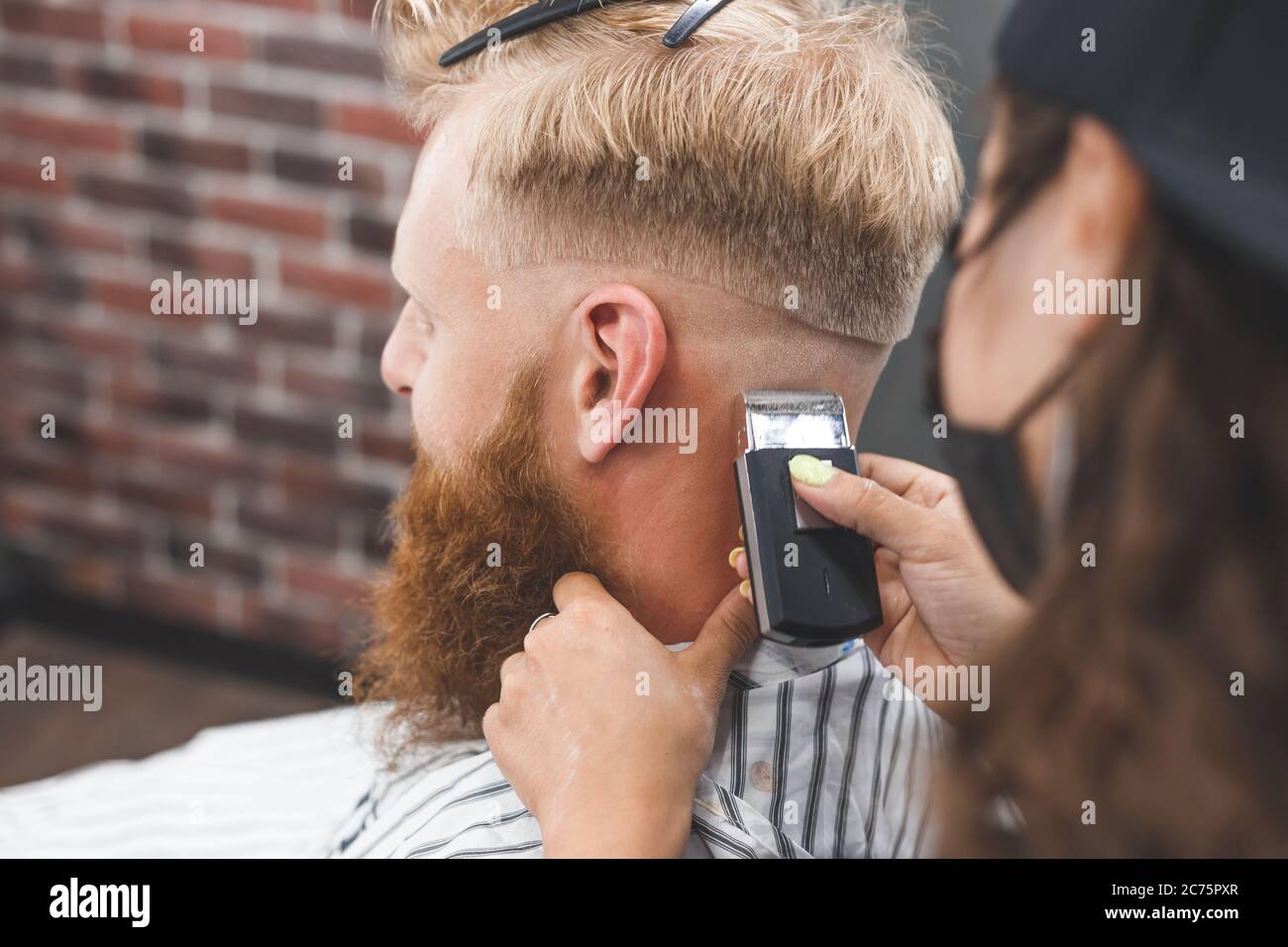 El hombre está cortando el pelo en una peluquería. Cuidado del cabello. Barbería en máscara de protección contra virus. Corte de pelo en cuarentena Foto de stock