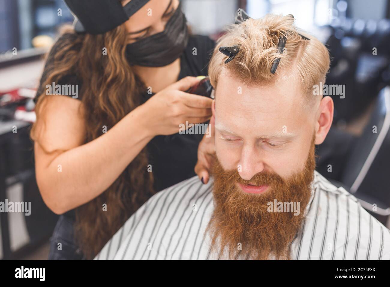Corte de pelo para hombre en una peluquería. Cuidado del cabello. Barbería en máscara de protección contra virus. Corte de pelo en cuarentena. Foto de stock