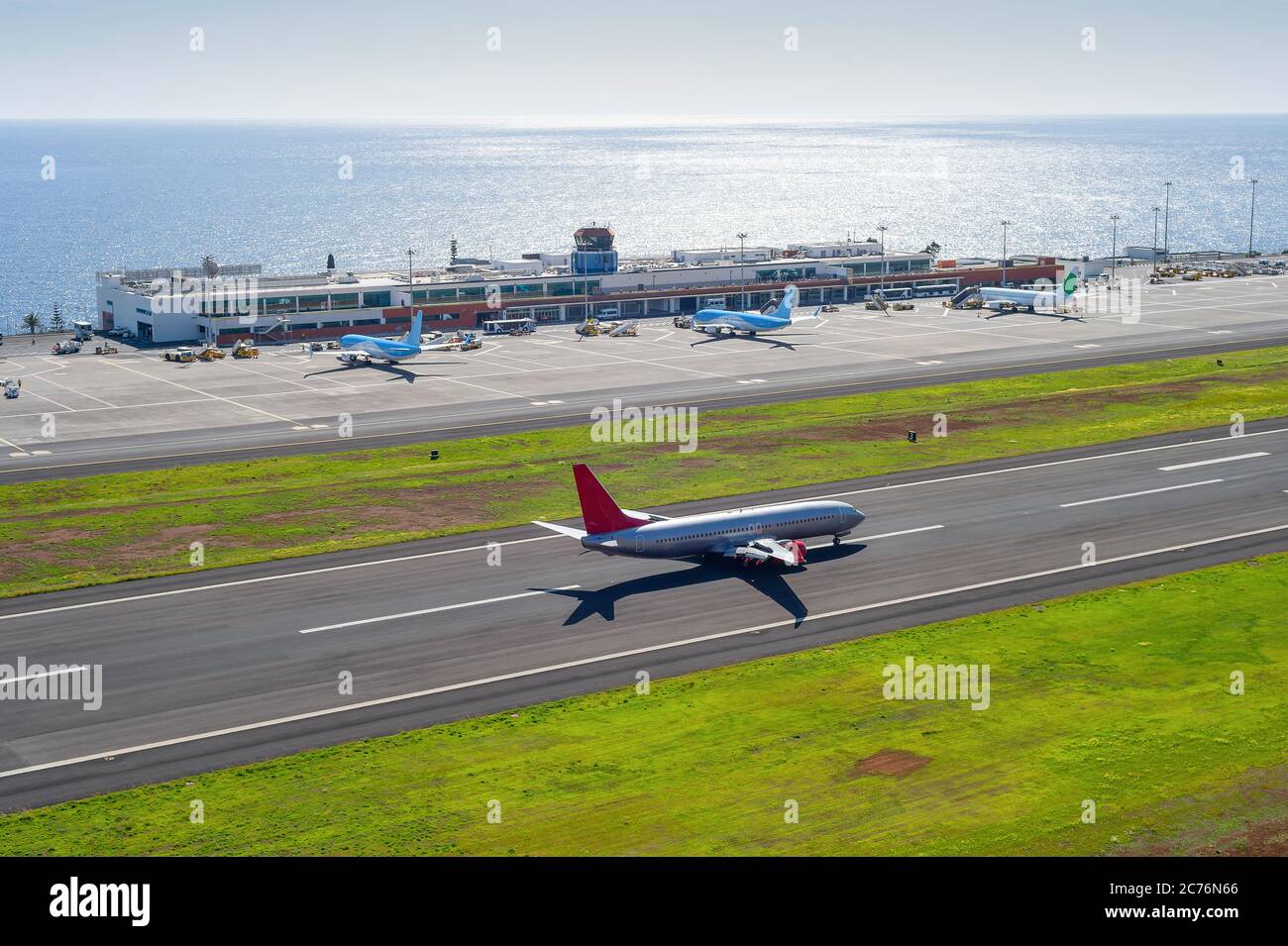 Vista aérea del aeropuerto internacional de Funchal con aviones por construcción de terminal, avión despegando en el campo aéreo, paisaje marino en el fondo con brillantes soles Foto de stock