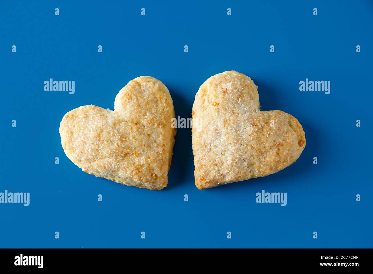 Galletas de azúcar en forma de corazón sobre un fondo azul. Dos galletas de azúcar en forma de corazón sobre un fondo azul, color de tendencia del año Foto de stock