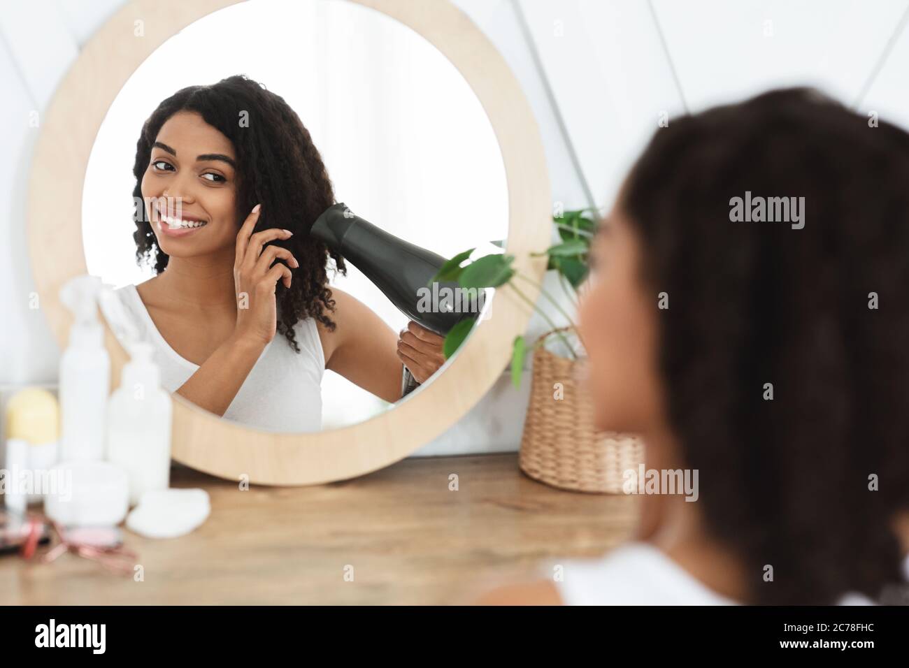 Hermosa mujer negra secado pelo rizado con secador de pelo en frente de  espejo Fotografía de stock - Alamy
