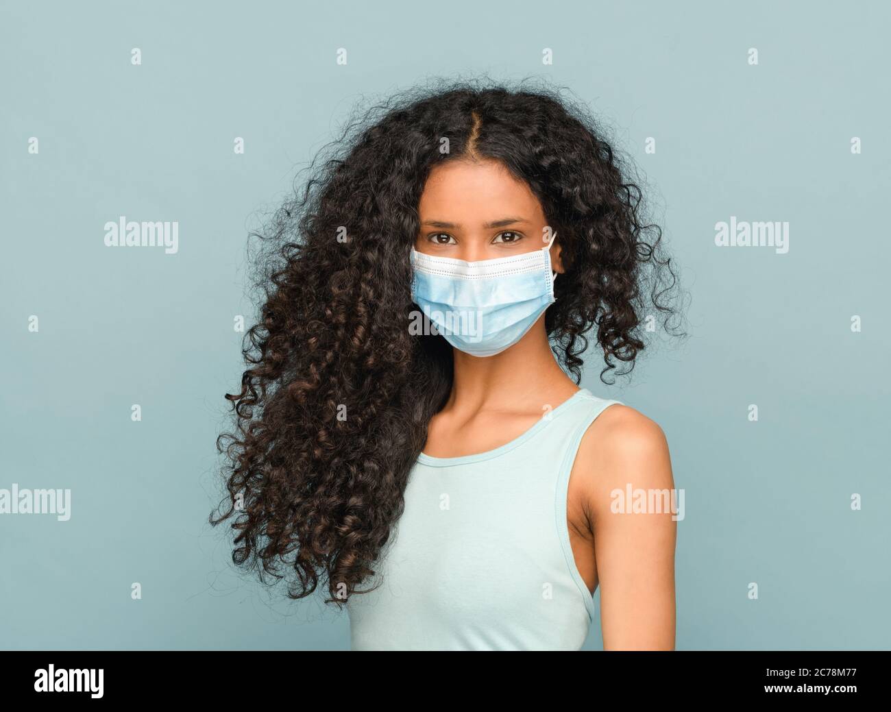Joven afro-americana con pelo largo rizado negro que lleva una máscara facial como protección contra el coronavirus o Covid-19 durante la pandemia en un saludable Foto de stock