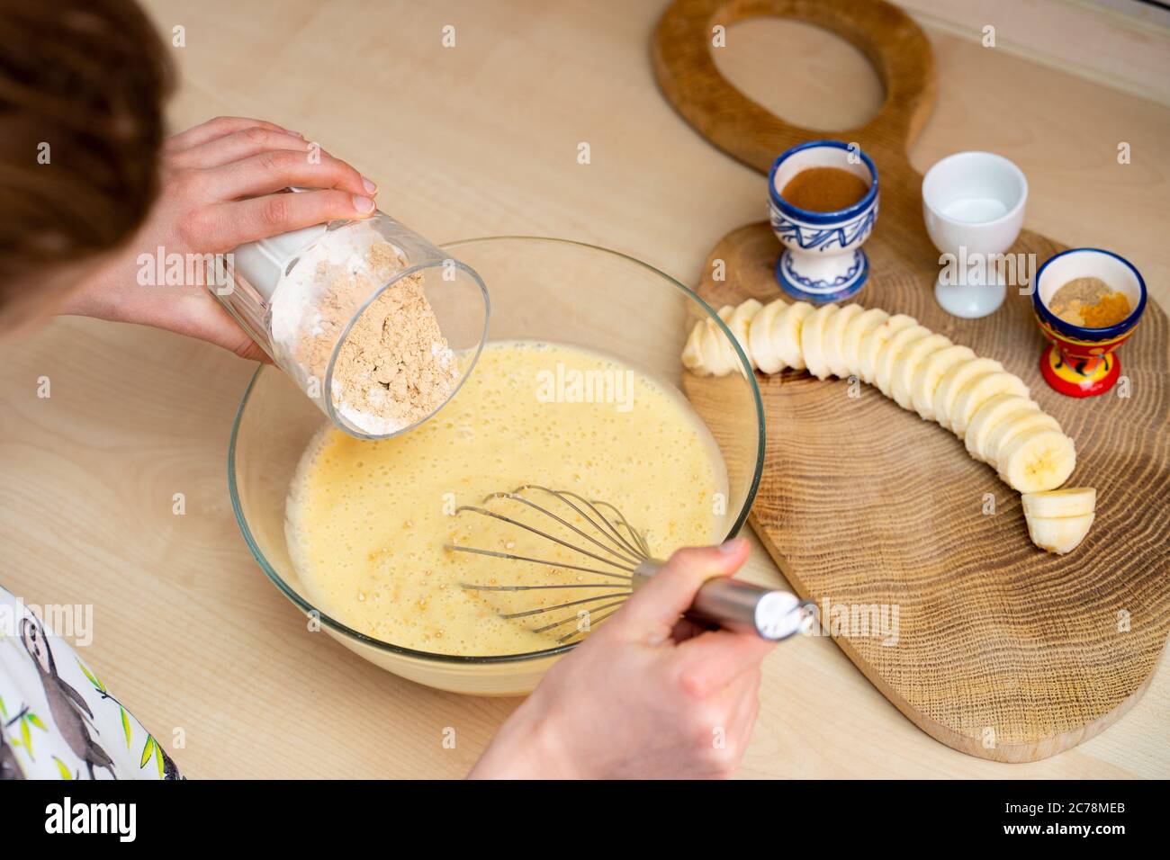 La niña sostiene un vaso con harina y prepara, fácil de hacer y saludable, pan casero de plátano. Foto de stock