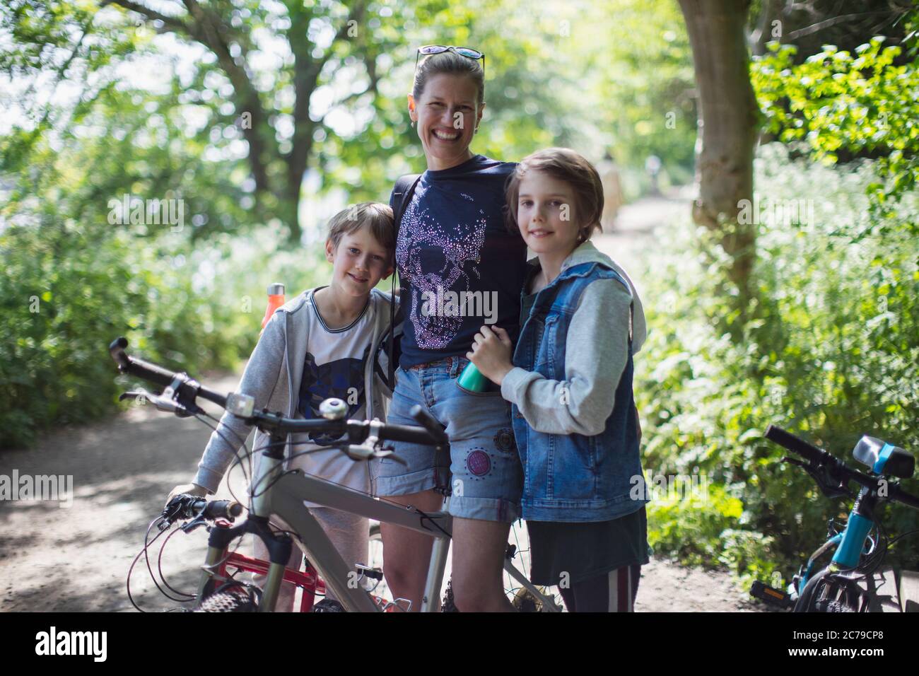 Retrato feliz madre e hijos disfrutando de un paseo en bicicleta en el parque soleado Foto de stock
