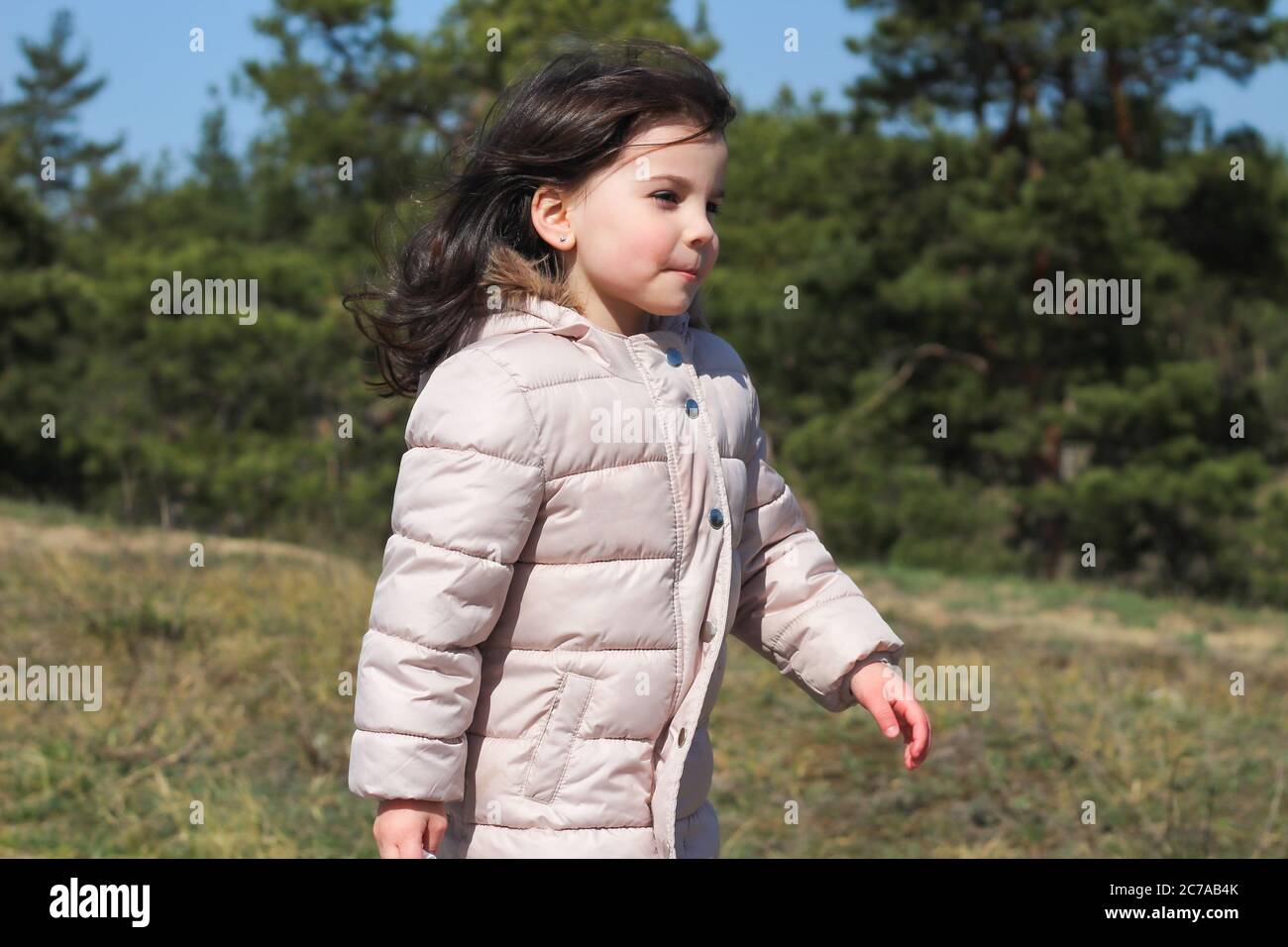 Una niña en una chaqueta larga cálida camina a lo largo de un camino de  asfalto hacia el viento en un parque Fotografía de stock - Alamy