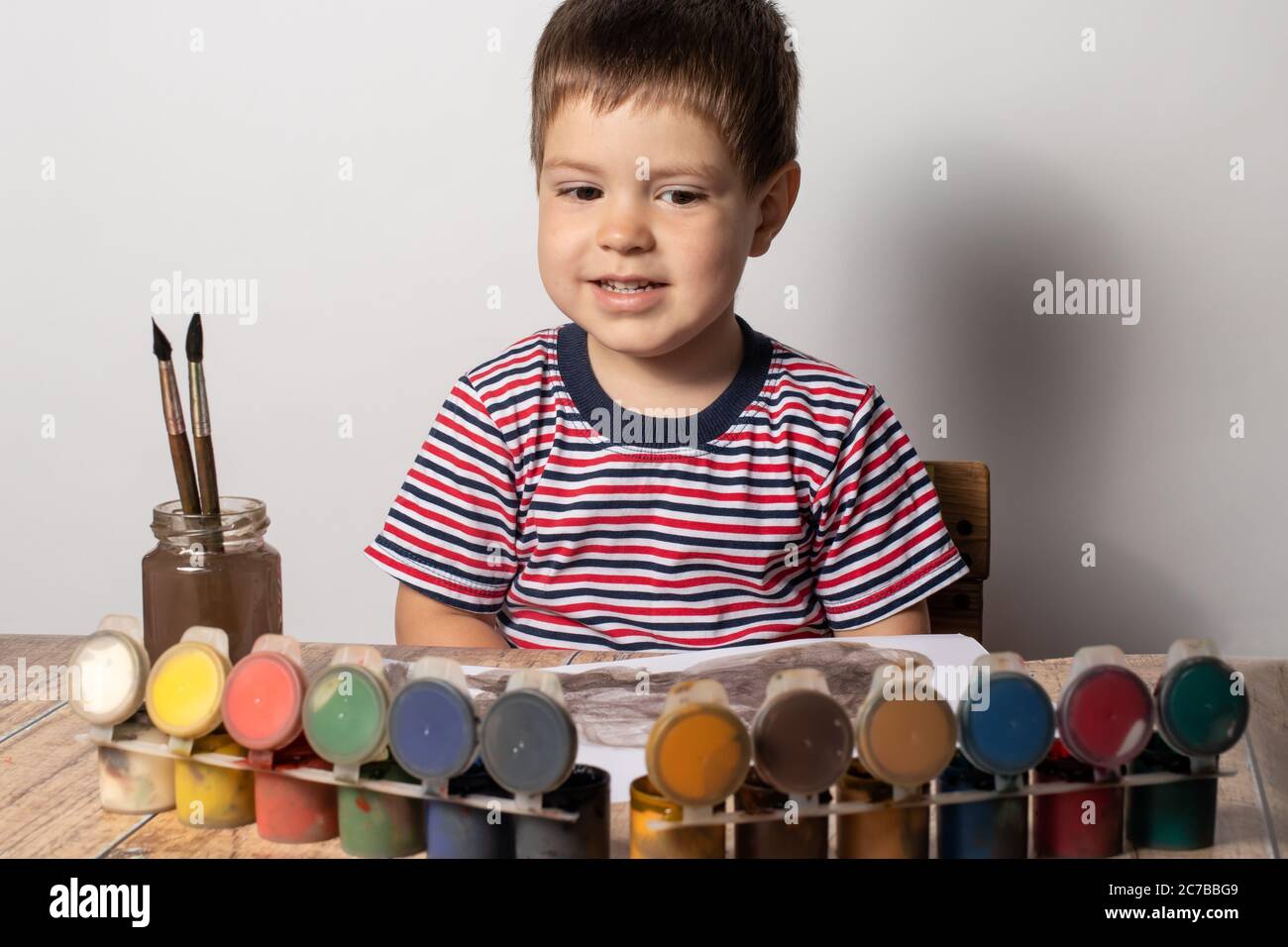 Un niño de 2-3 años en una camiseta de rayas multicolor dibuja guasya  pinturas en papel. Ocio y entretenimiento para niños, desarrollo infantil  Fotografía de stock - Alamy