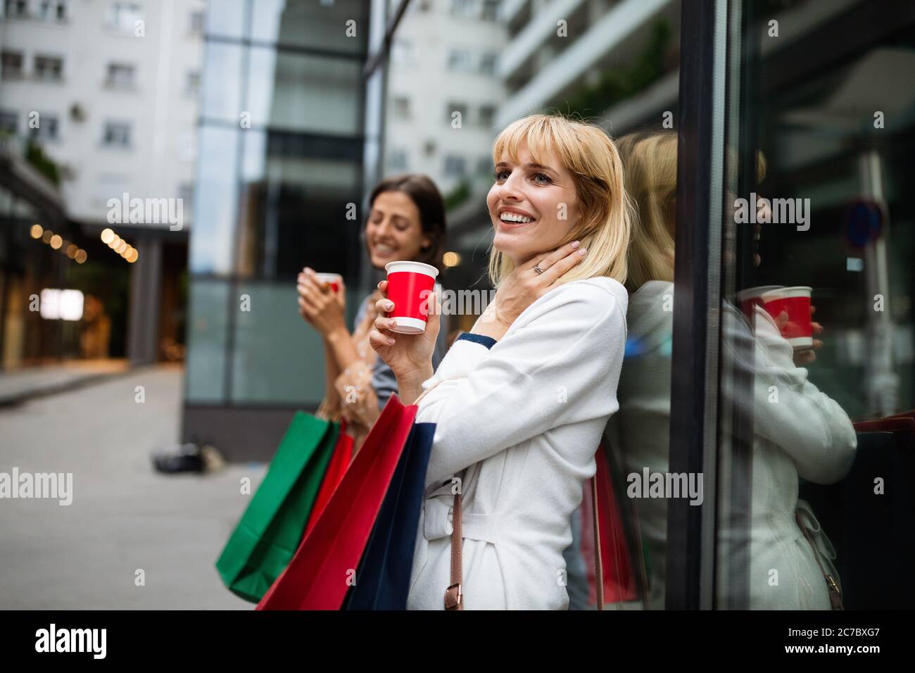 Feliz mujer joven bebiendo tomar café y caminar con bolsas después de ir de compras en la ciudad. Foto de stock
