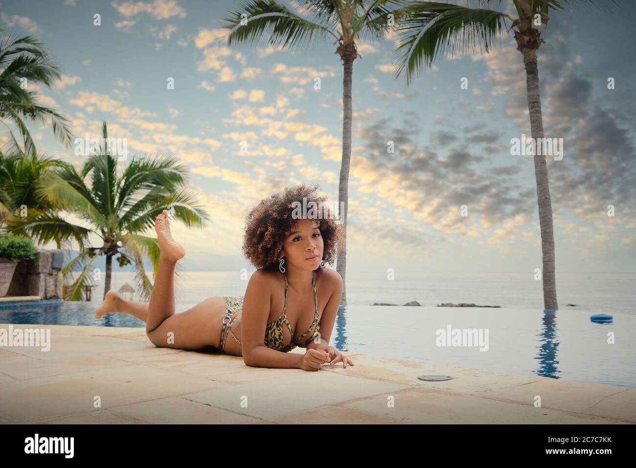 Bonita mujer en bikini bronceándose en la piscina, Puerto Vallarta, México - Mujer joven con pelo de mirada afro disfrutando de un día de vacaciones en la piscina Foto de stock