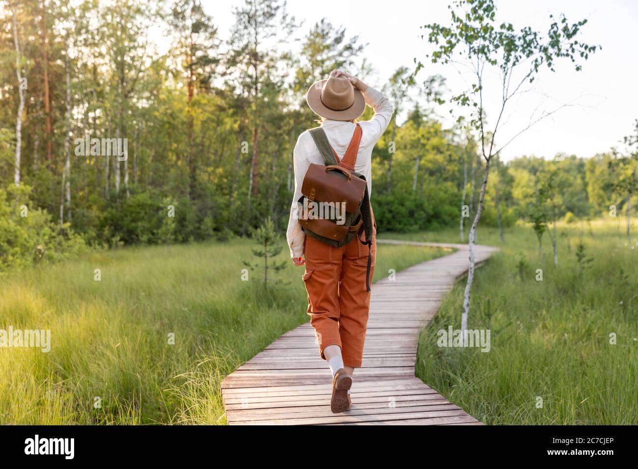 Mujer botánica con mochila en sendero ecológico en verano al aire libre. Naturalista explorando la vida silvestre y ecoturismo aventura caminando por el camino Foto de stock