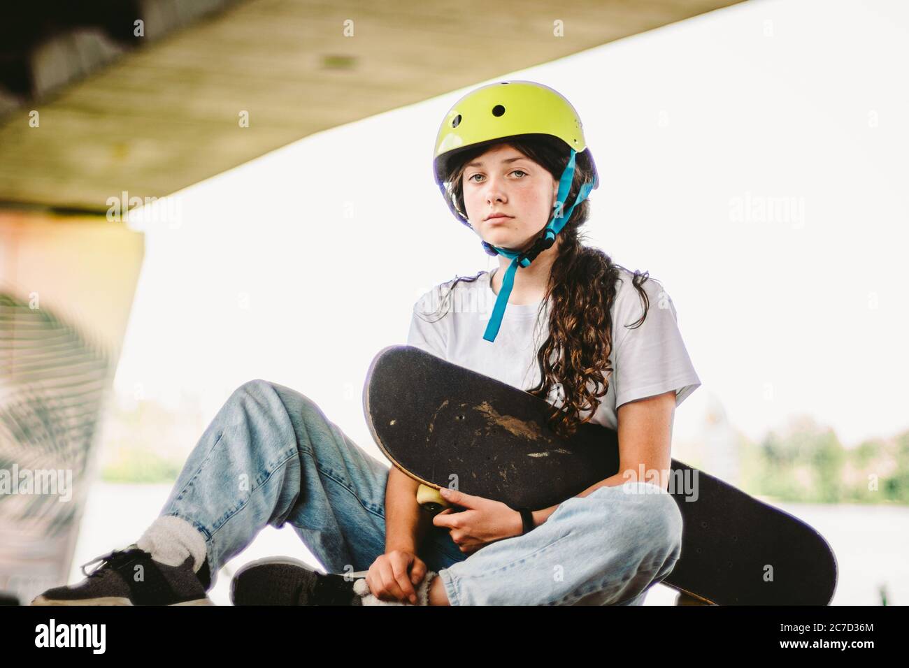 Niña adolescente en casco y ropa con estilo posando en la rampa de media  pipa un parque de patinaje al aire libre. Hermoso niño mujer modelo  skatboarder con tabla de skate en