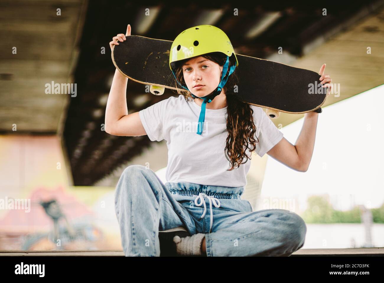 Niña adolescente en casco y ropa con estilo posando en la rampa de media pipa un parque patinaje al aire libre. Hermoso niño modelo skatboarder con tabla de skate en