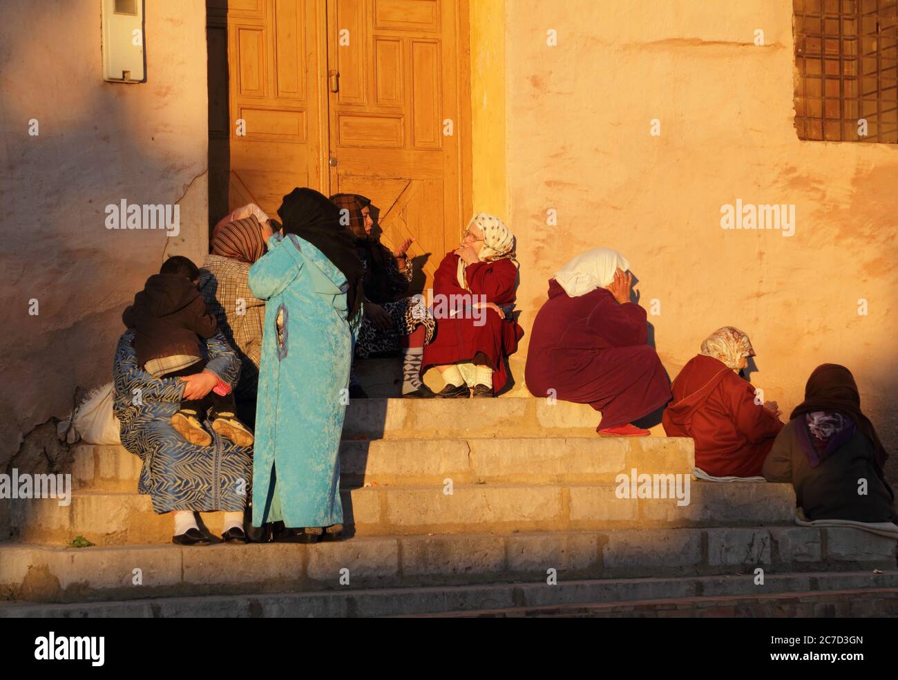 Un grupo de mujeres marroquíes típicamente vestidas sentadas en escalones bajo el sol de invierno de la tarde. 22 de diciembre de 2013 en Meknes, Marruecos. Sitio de la UNESCO. Foto de stock