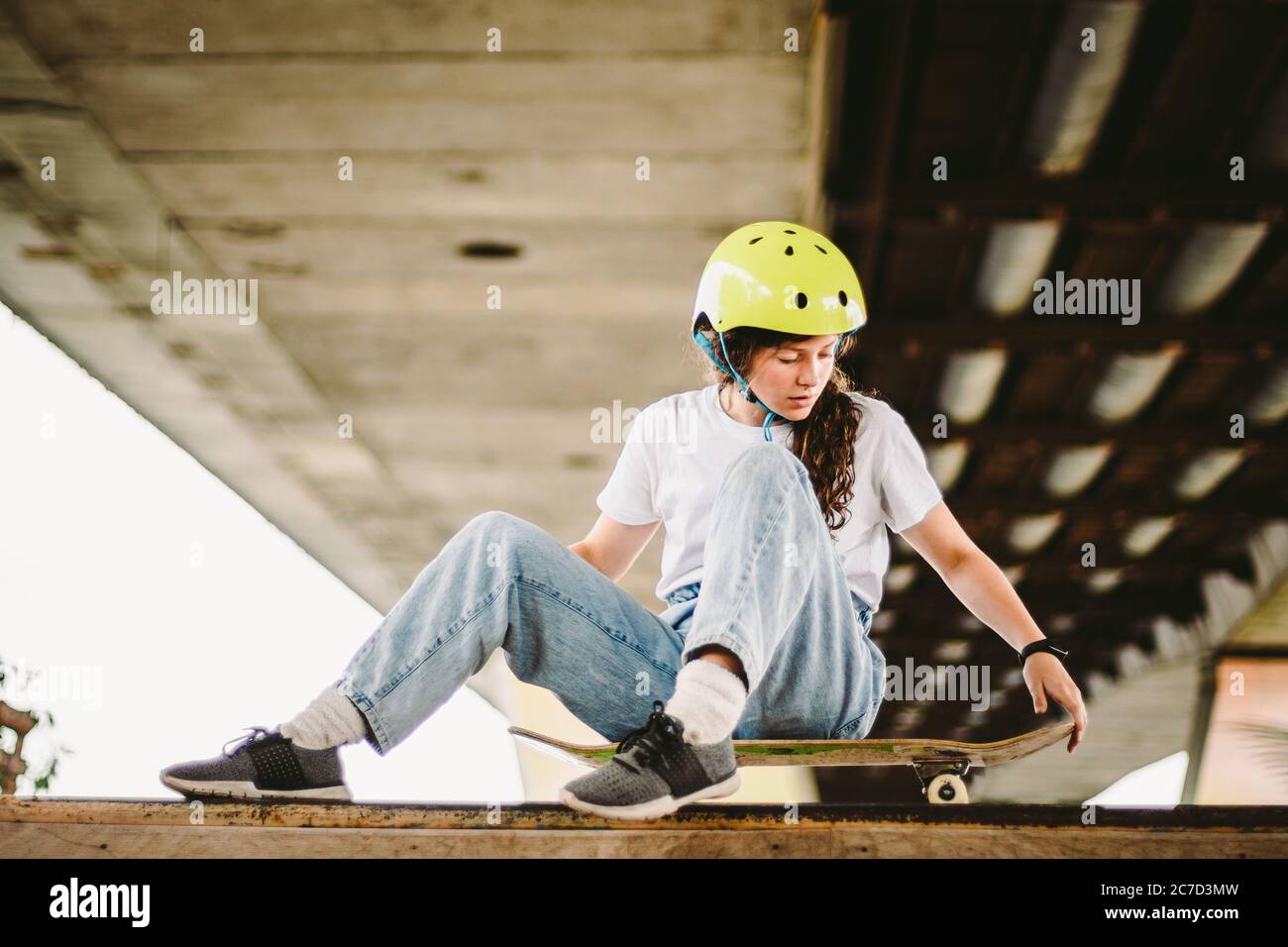 Niña adolescente en casco y ropa con estilo posando en la rampa de media pipa un parque patinaje al aire libre. Hermoso niño modelo skatboarder con tabla de skate en