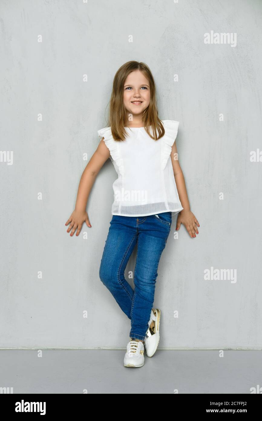 Niña en blusa blanca y jeans inclinados a la pared en el estudio Fotografía  de stock - Alamy
