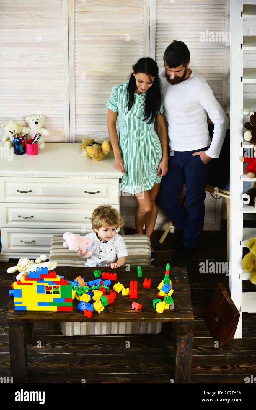 Padres e hijo con cara curiosa jugando con juguetes. Amor y juegos de  familia. Mamá y papá ven a su hijo jugar con bloques de colores sobre el  fondo de la habitación.