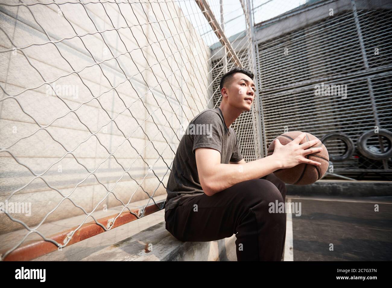 joven asiático hombre jugador de baloncesto sentado en el patio Foto de stock
