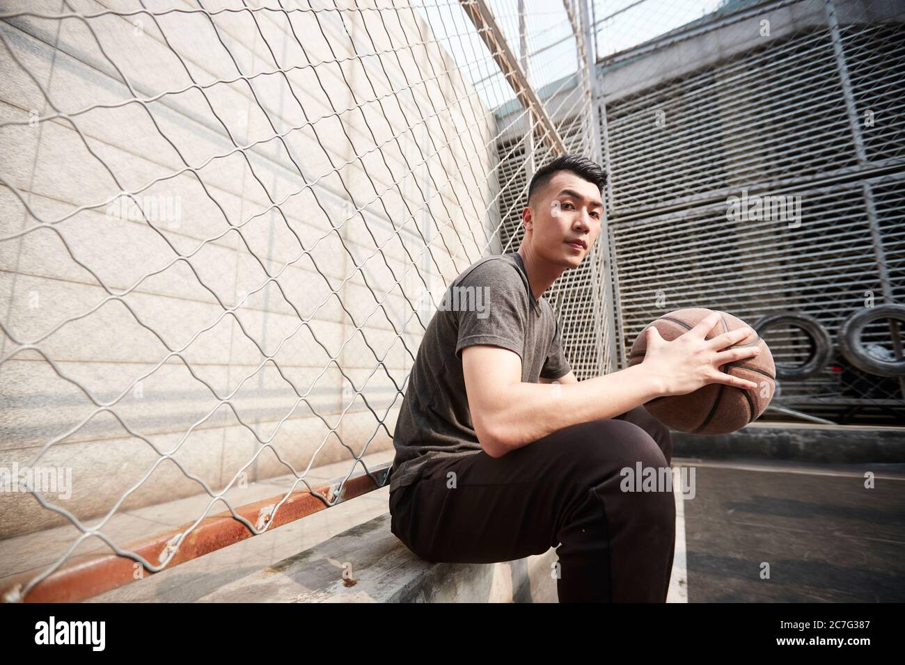joven asiático hombre jugador de baloncesto sentado en el patio Foto de stock