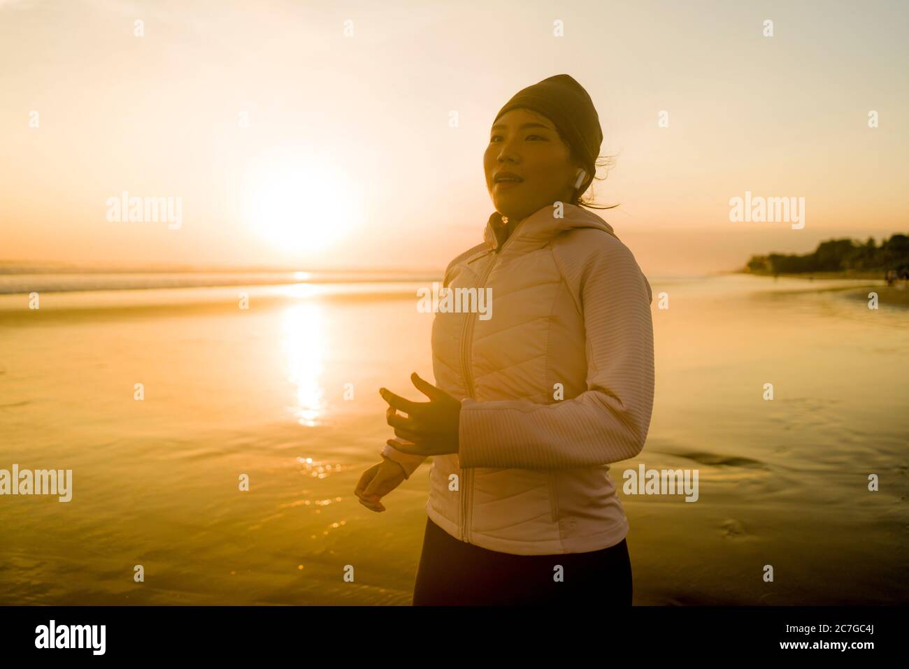 Chica asiática corriendo en la playa - joven atractiva y feliz China haciendo ejercicio de jogging en la hermosa playa disfrutando de la aptitud y el runas saludable Foto de stock