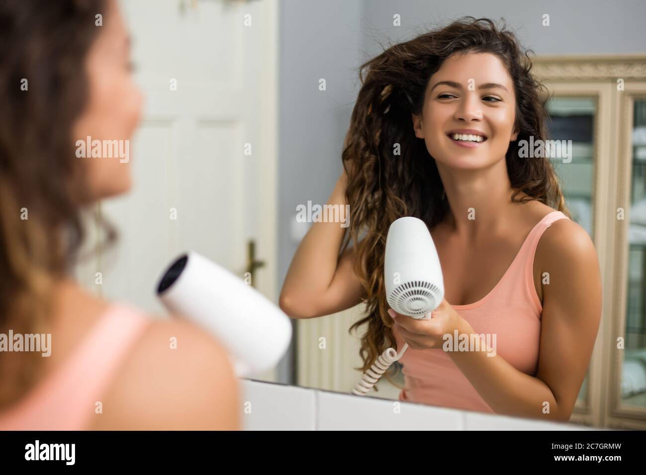 Mujer joven feliz con secador de pelo después de su cabello rizado
