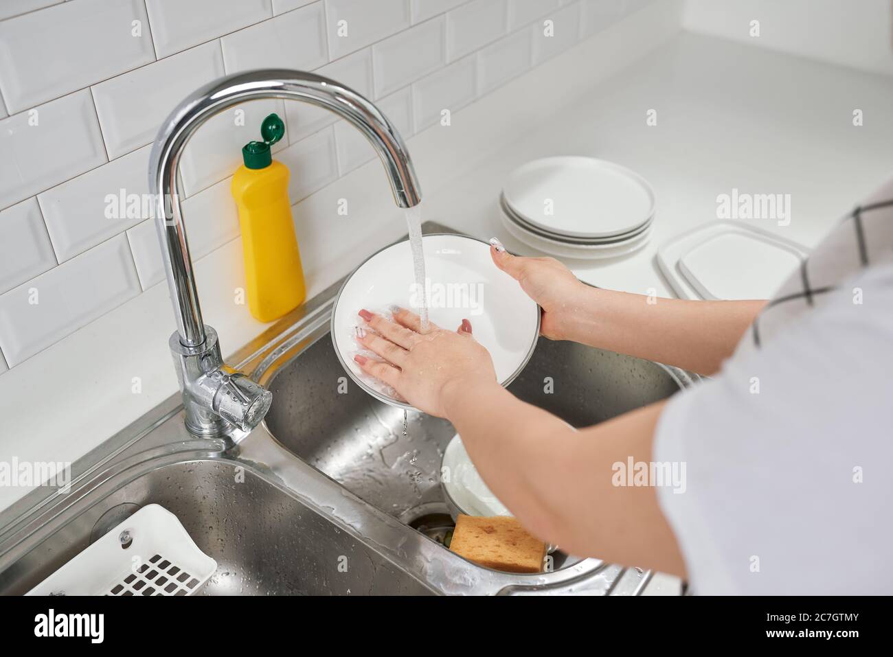 Mujer manos enjuagando platos bajo el agua corriente en el fregadero Foto de stock