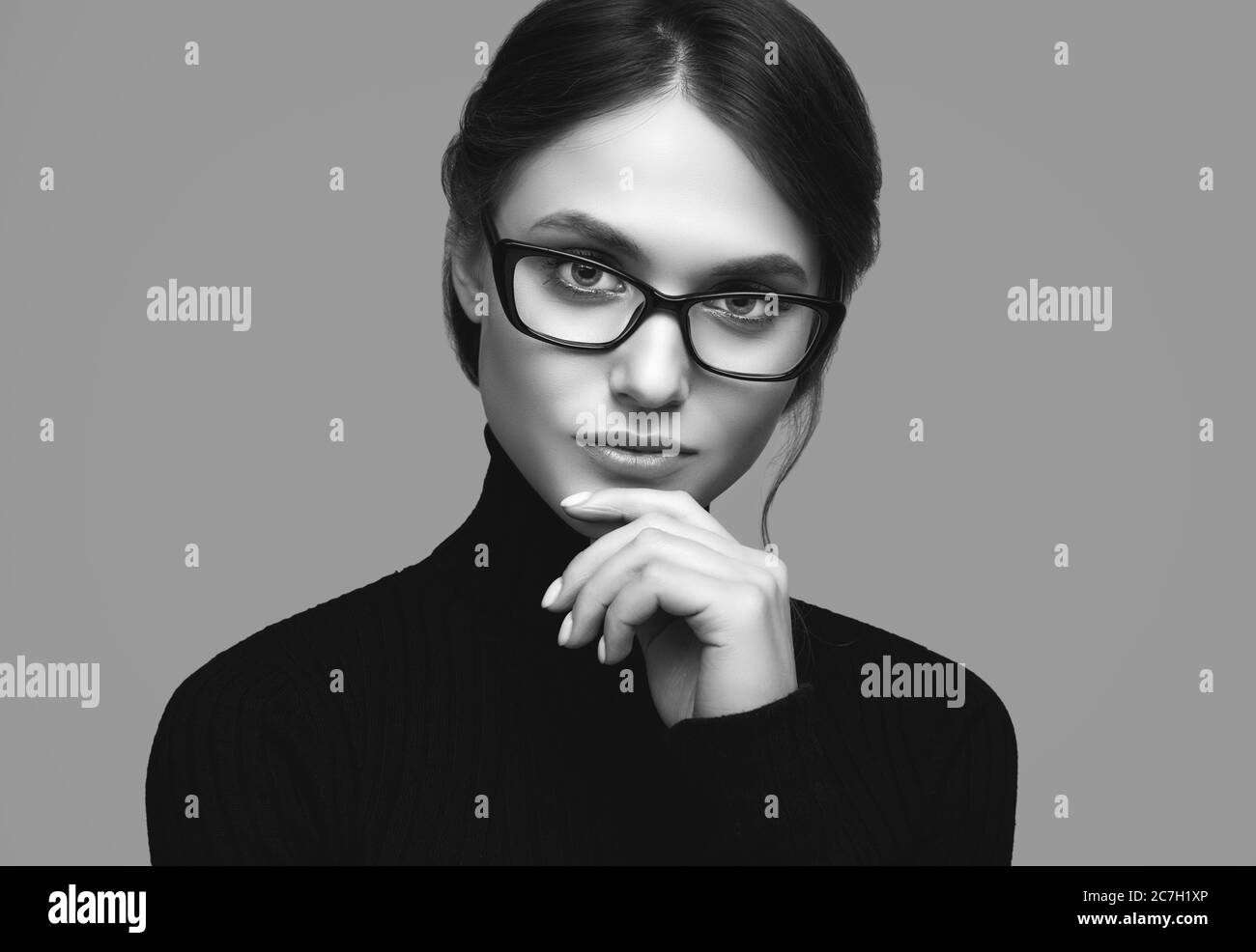 Retrato de una chica linda con un suéter de cuello turtleneck negro y gafas con estilo posando sobre fondo gris en el estudio Foto de stock