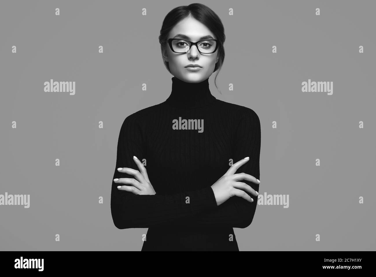 Retrato de una chica linda con un suéter de cuello turtleneck negro y gafas con estilo posando sobre fondo gris en el estudio Foto de stock