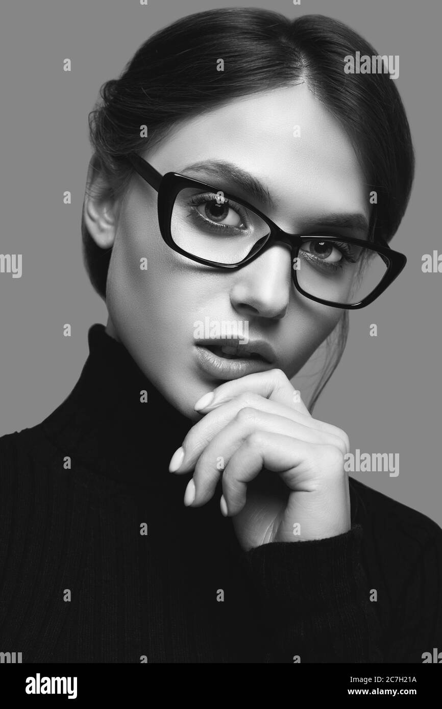 Retrato de una chica linda con un suéter de cuello turtleneck negro y gafas con estilo posando sobre fondo gris en el estudio Foto de stock