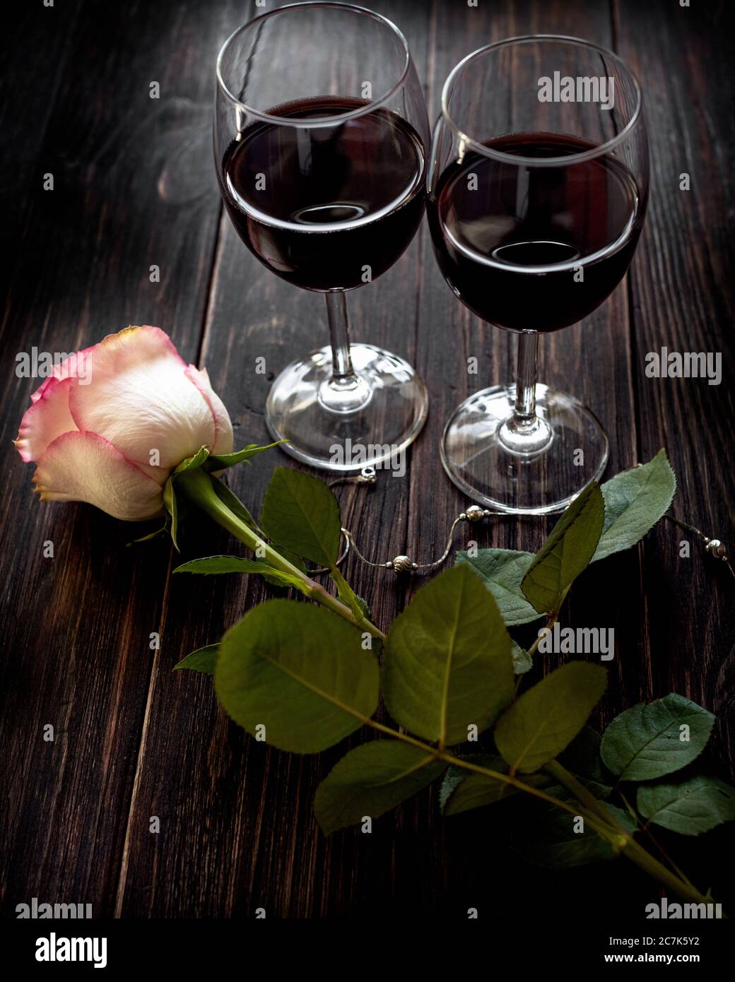 Dos copas de vino tinto y una rosa situadas en una mesa de madera de época  Fotografía de stock - Alamy