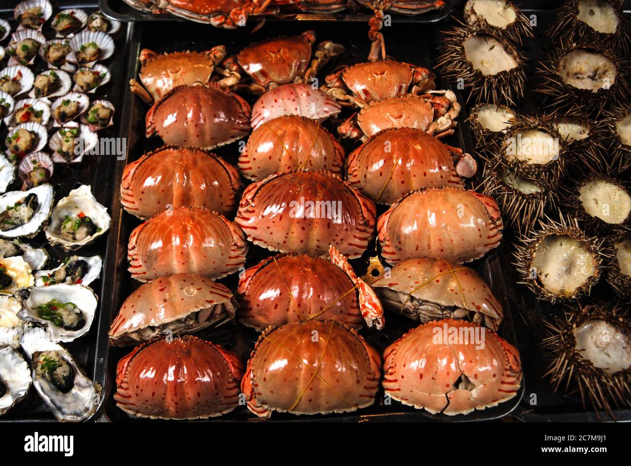 Una vista sobre un tallo asiático del mercado lleno de erizos de mar rojos, cangrejos, almejas y mariscos. Foto de stock