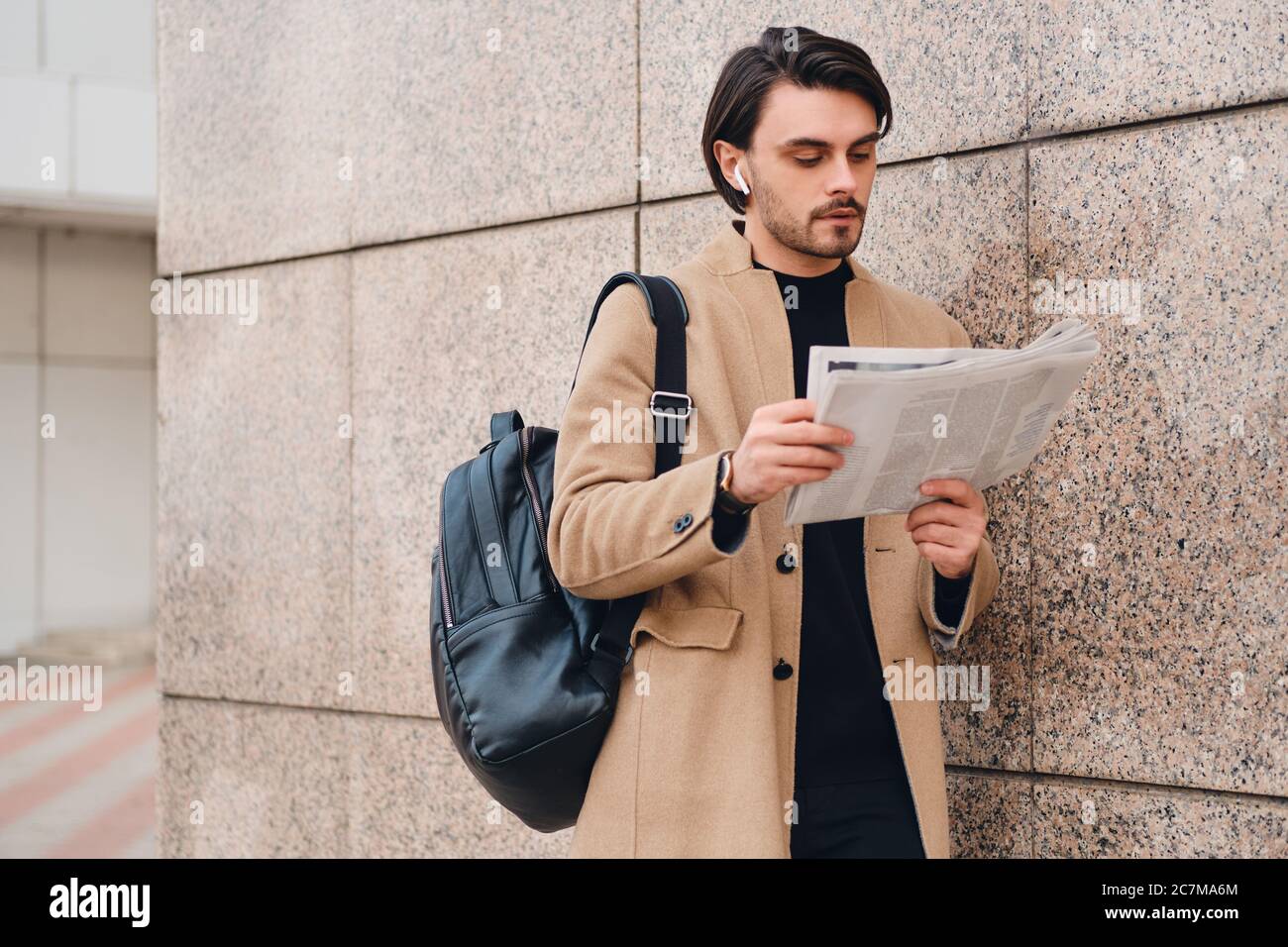 Joven hombre informal en abrigo beige con mochila leyendo el periódico al  aire libre Fotografía de stock - Alamy