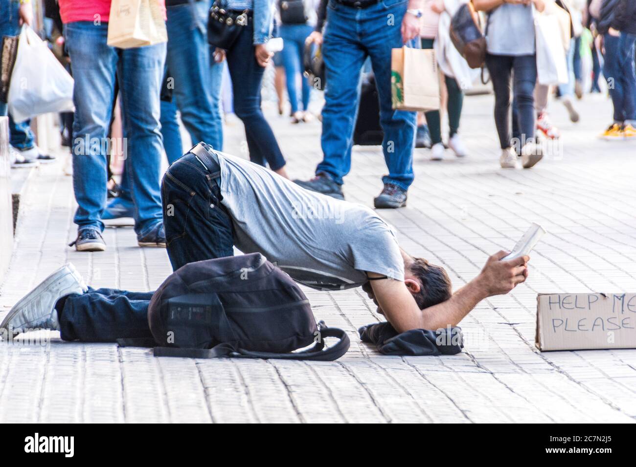 Un joven sin hogar con un respaldo con un signo que dice, 'Ayuda por favor,' Barcelona, España. Foto de stock