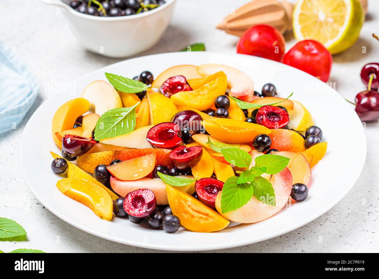Ensalada de frutas con bayas en un plato blanco, fondo blanco. Concepto de comida vegetariana saludable. Foto de stock