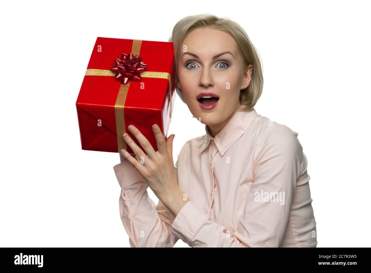 Mujer sorprendida con la boca abierta poniendo su oído al presente en papel rojo. Foto de stock