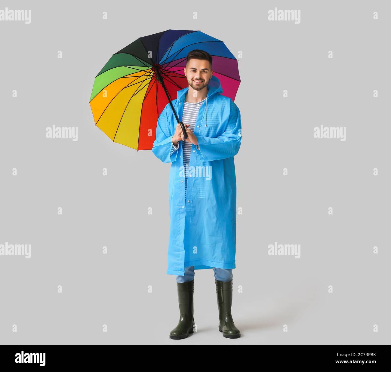 Joven en impermeable y con paraguas sobre fondo claro Foto de stock