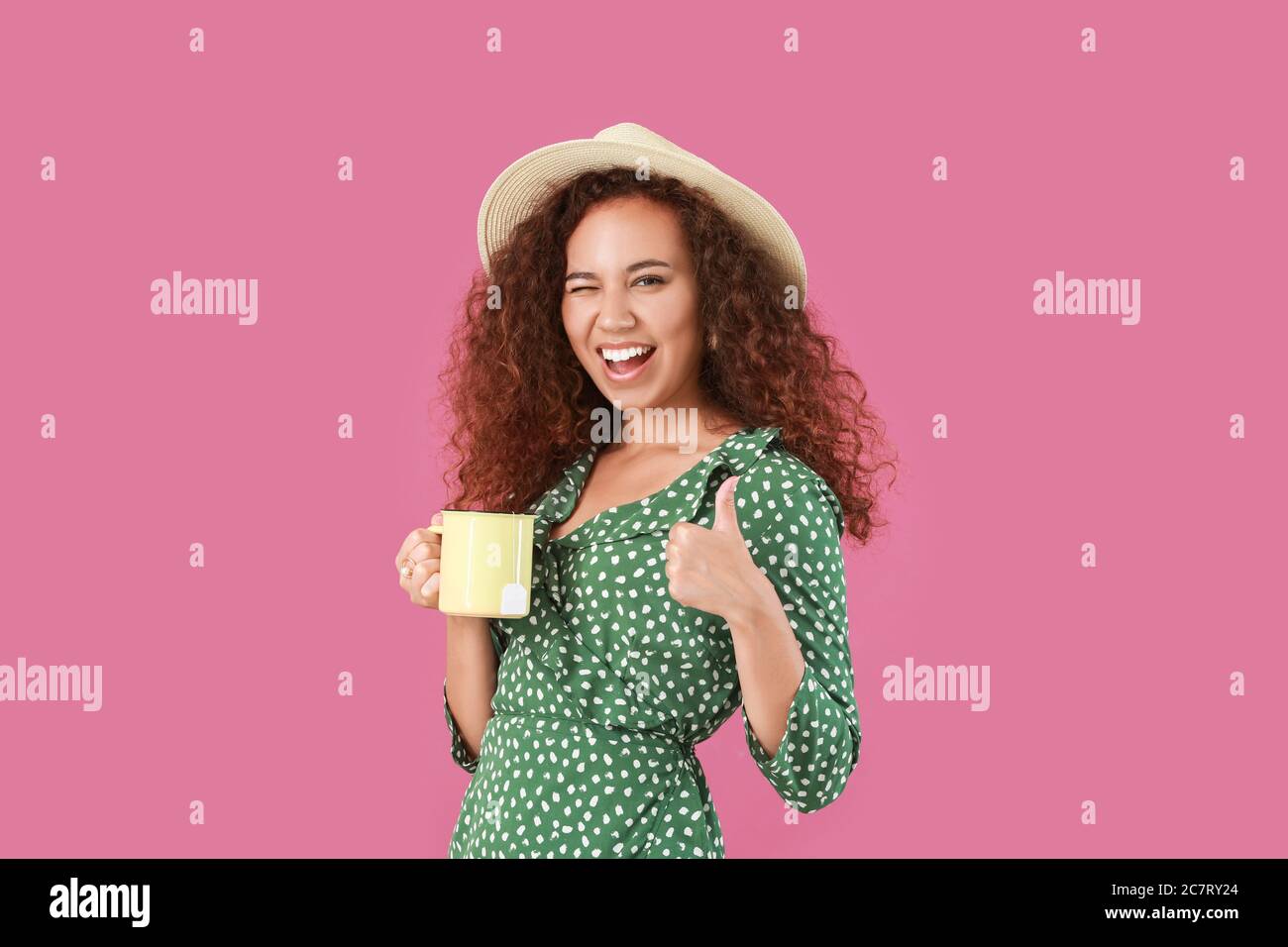 Hermosa joven afroamericana con té caliente mostrando pulgar-hacia arriba sobre fondo de color Foto de stock
