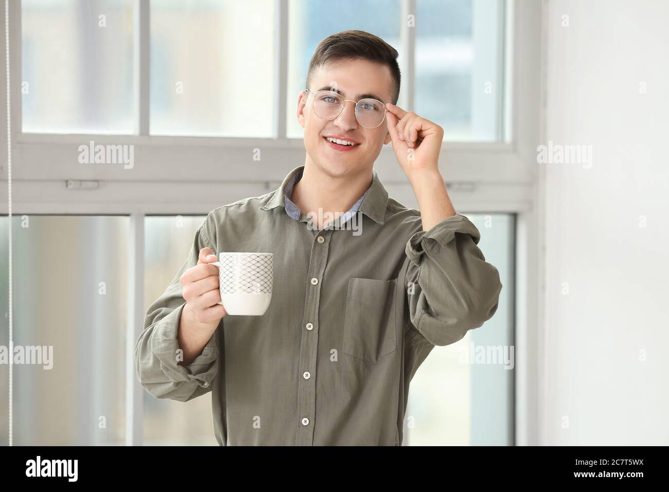 Un hombre joven guapo bebiendo té cerca de la ventana en casa Foto de stock