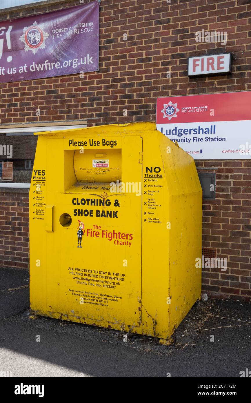 Banco de reciclaje de ropa y calzado (depósito de metal amarillo) fuera de una estación de bomberos para recaudar dinero para la organización benéfica de bomberos, Reino Unido Foto de stock
