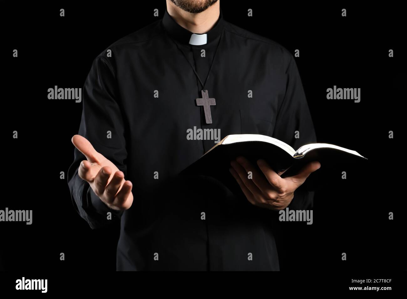 Un sacerdote guapo con la Biblia sobre fondo oscuro Foto de stock