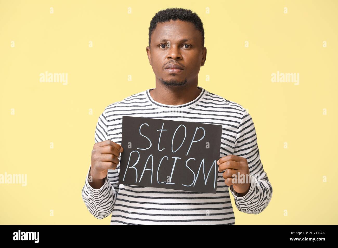 Triste hombre afroamericano con cartel sobre fondo de color. Detener el racismo Foto de stock