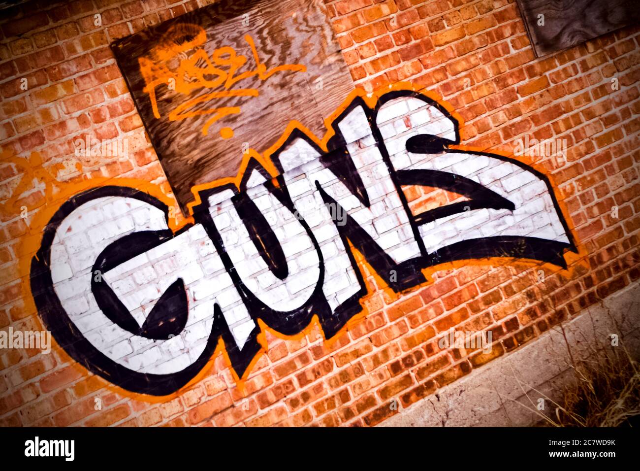 Armas" deletreado en grandes letras de graffiti en una pared de ladrillo  rojo con una ventana con un panel. Colores blanco, naranja brillante y  neutro. Palabras en las paredes Fotografía de stock -