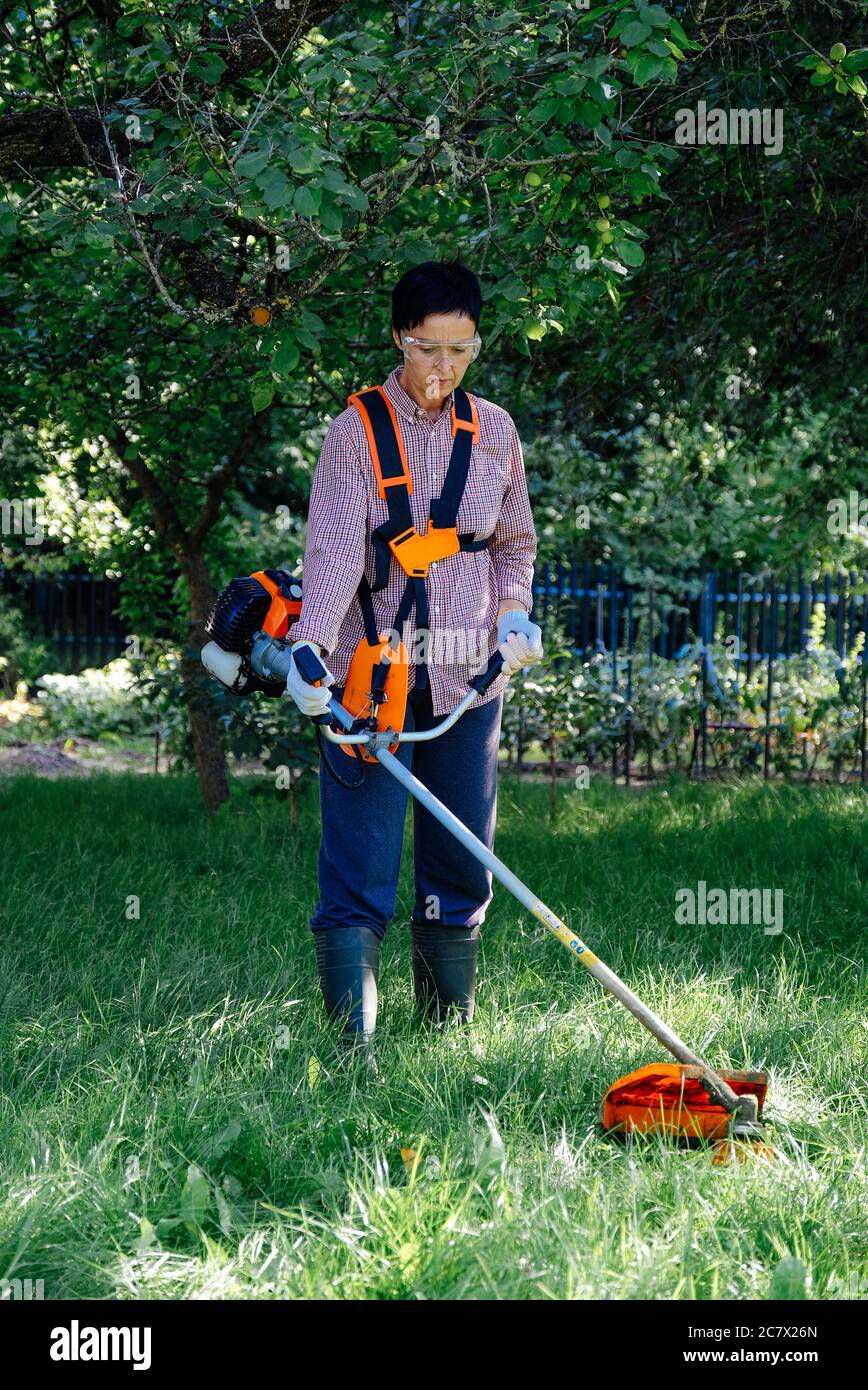 La mujer adulta siembra la hierba en el patio trasero usando un cortapatillas. Concepto de trabajo en el jardín. Foto de stock