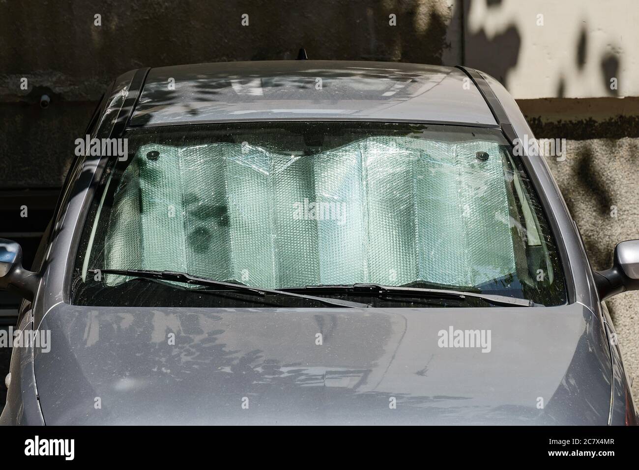 Sol de aluminio se pone bajo el parabrisas de un coche gris estacionado al  aire libre en un soleado día de verano. Protector solar reflectante de  aluminio plateado metálico Fotografía de stock -