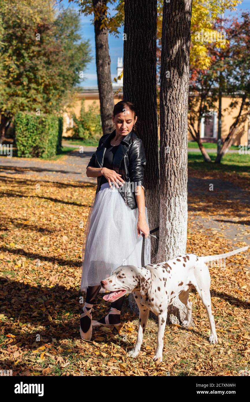 Bailarina con perro dálmata en el parque. Mujer bailarina de ballet en un  blanco de la falda y la chaqueta de cuero negro bailando en Pointe zapatos  en otoño parque con Fotografía