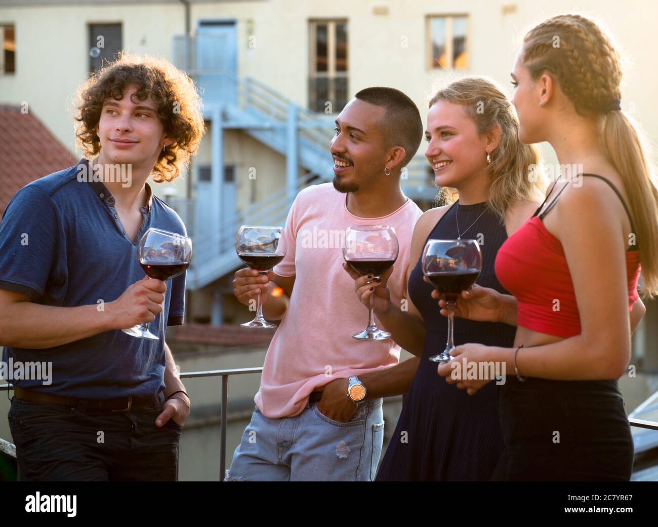Cuatro niños pequeños tostar con una copa de vino al atardecer en la terraza Foto de stock