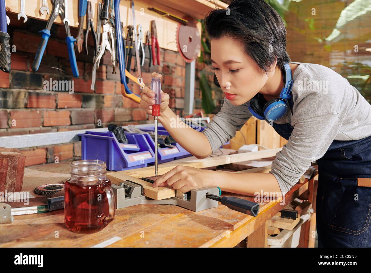 Carpintero femenino vietnamita concentrado usando destornillador y tornillo  de banco para unir tablas de madera Fotografía de stock - Alamy