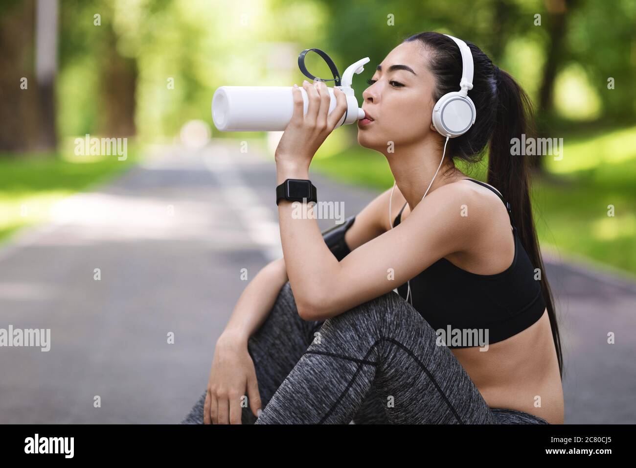 Sed después del entrenamiento. Joven asiática bebiendo agua, descansando después de correr fuera de los sóores Foto de stock